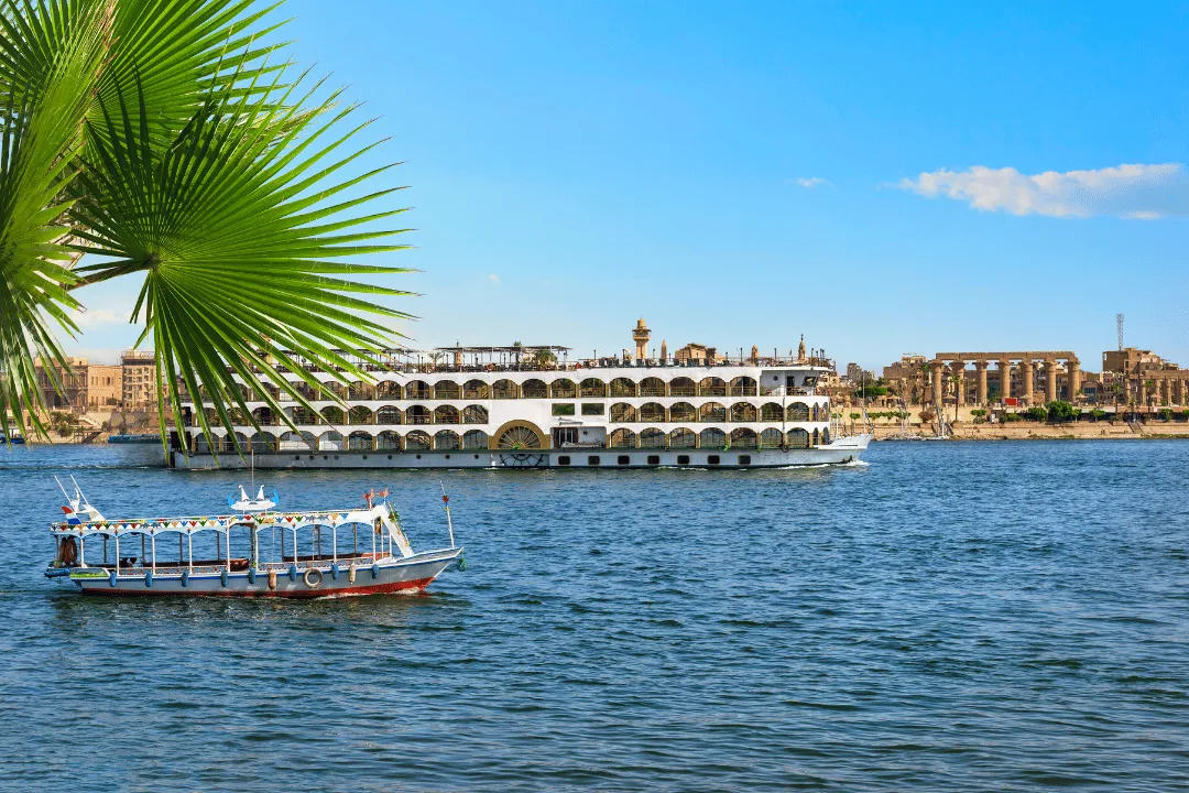 A Nile cruise ship passing the floodlit columns of Luxor Temple at night
